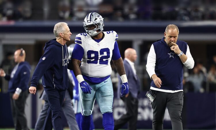 Dallas Cowboys defensive tackle Quinnen Williams walks off the field flanked by two team trainers.