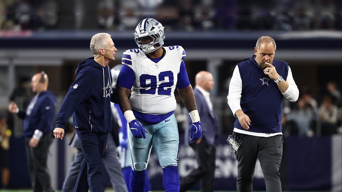 Dallas Cowboys defensive tackle Quinnen Williams walks off the field flanked by two team trainers.