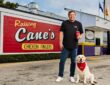 Raising Cane's founder Todd Graves stands with a yellow Labrador outside the original Raising Cane's restaurant.
