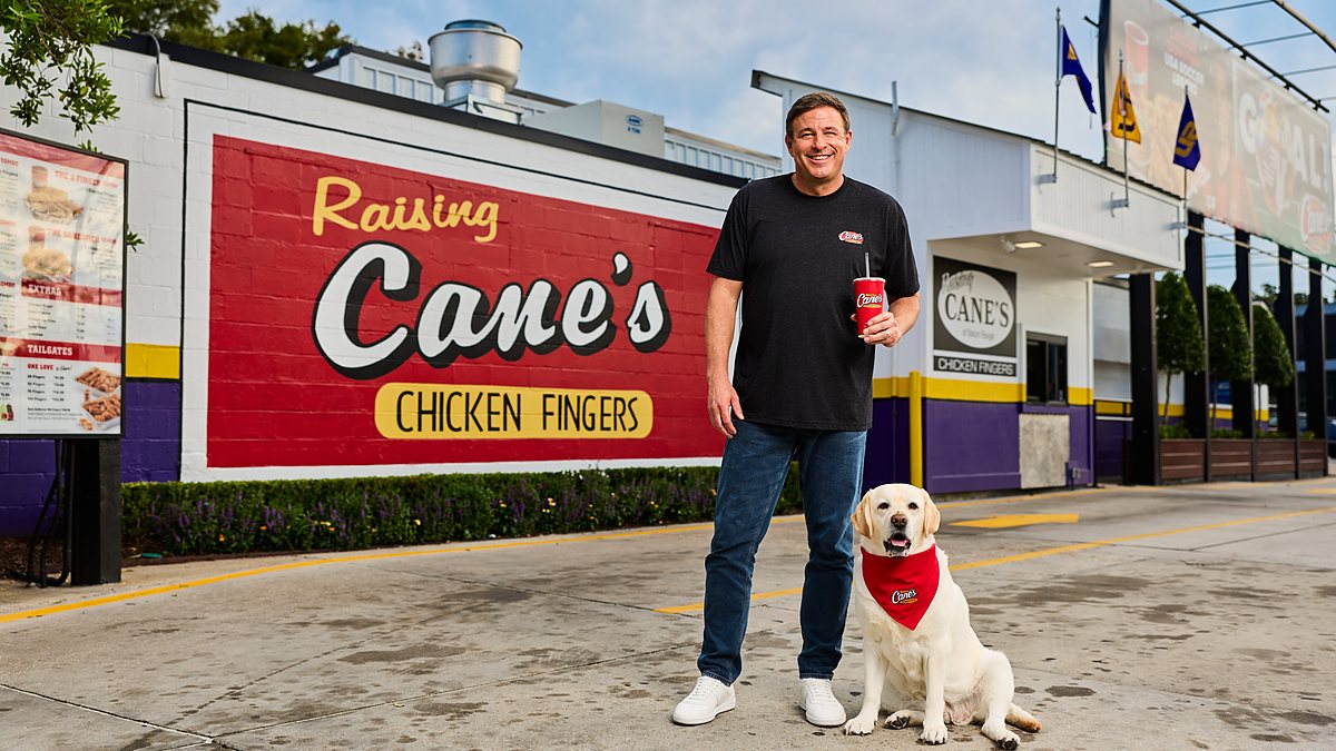 Raising Cane's founder Todd Graves stands with a yellow Labrador outside the original Raising Cane's restaurant.