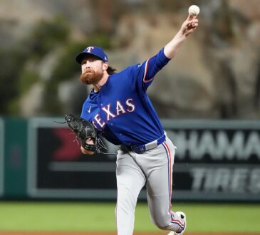 A Texas Rangers relief pitcher throws from the mound in a gray road uniform at Angel Stadium.