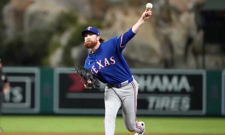 A Texas Rangers relief pitcher throws from the mound in a gray road uniform at Angel Stadium.