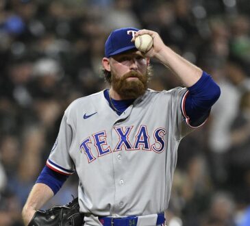 Texas Rangers pitcher Robby Ahlstrom holds the ball up near his cap on the mound in a gray road uniform.