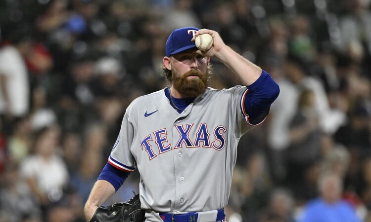 Texas Rangers pitcher Robby Ahlstrom holds the ball up near his cap on the mound in a gray road uniform.