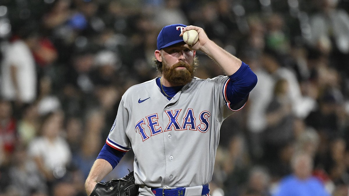 Texas Rangers pitcher Robby Ahlstrom holds the ball up near his cap on the mound in a gray road uniform.