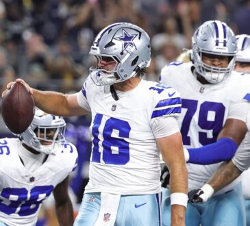 Dallas Cowboys quarterback Sam Howell holds up the ball to celebrate a two-point conversion as teammates gather behind him.