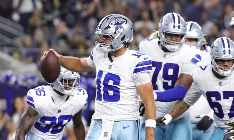 Dallas Cowboys quarterback Sam Howell holds up the ball to celebrate a two-point conversion as teammates gather behind him.