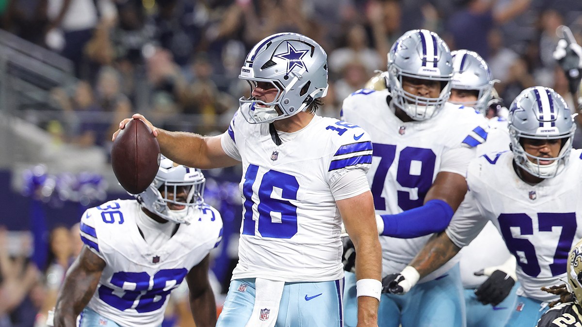 Dallas Cowboys quarterback Sam Howell holds up the ball to celebrate a two-point conversion as teammates gather behind him.