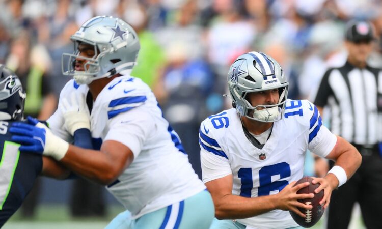 Dallas Cowboys quarterback Sam Howell holds the ball and scans downfield as a lineman blocks a Seattle Seahawks defender.