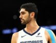 Memphis Grizzlies forward Santi Aldama looks toward the court in a white Memphis jersey with blue kinesiology tape on his shoulder.