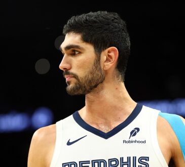 Memphis Grizzlies forward Santi Aldama looks toward the court in a white Memphis jersey with blue kinesiology tape on his shoulder.