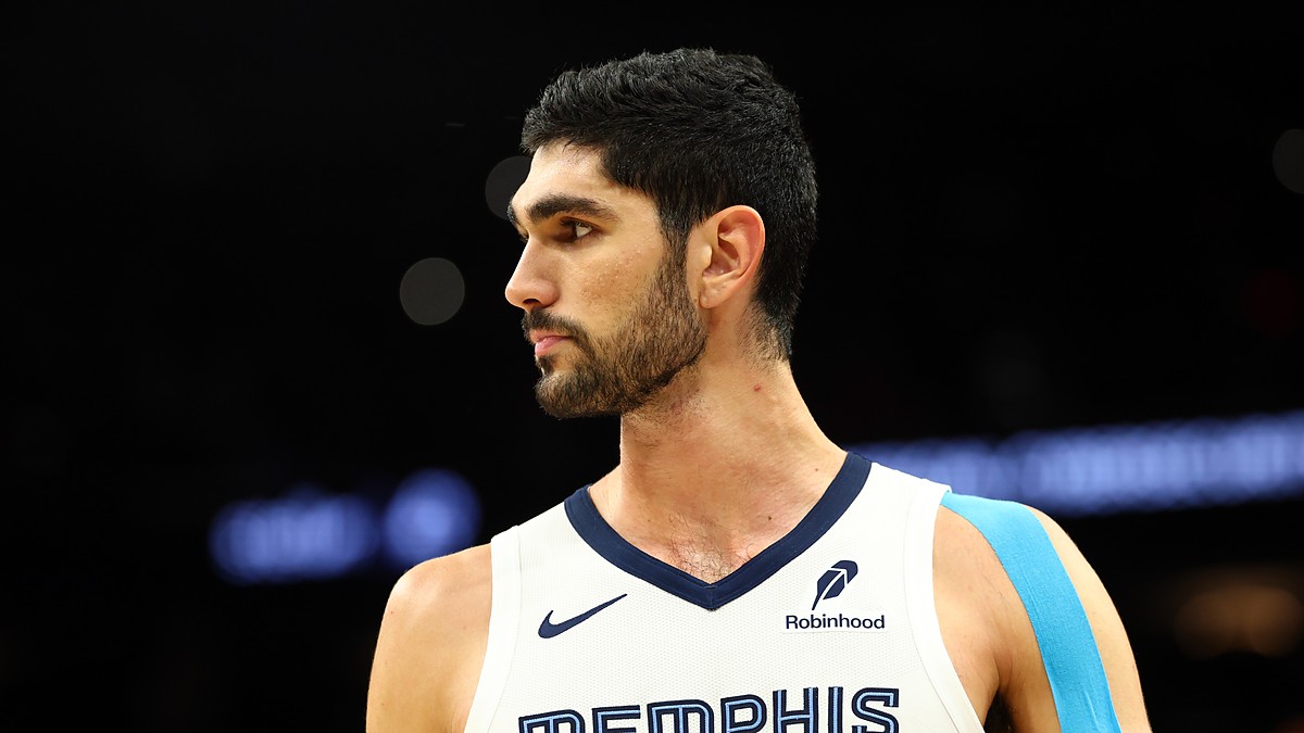 Memphis Grizzlies forward Santi Aldama looks toward the court in a white Memphis jersey with blue kinesiology tape on his shoulder.