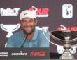 Scottie Scheffler smiles at a news conference podium next to the FedEx Cup trophy.