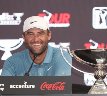 Scottie Scheffler smiles at a news conference podium next to the FedEx Cup trophy.