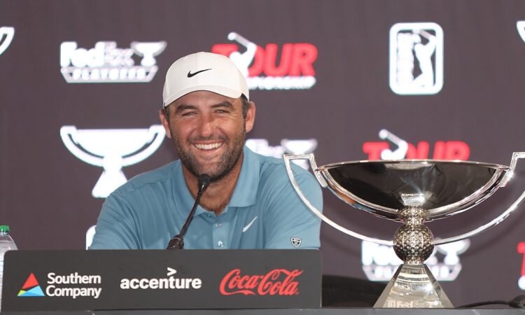 Scottie Scheffler smiles at a news conference podium next to the FedEx Cup trophy.