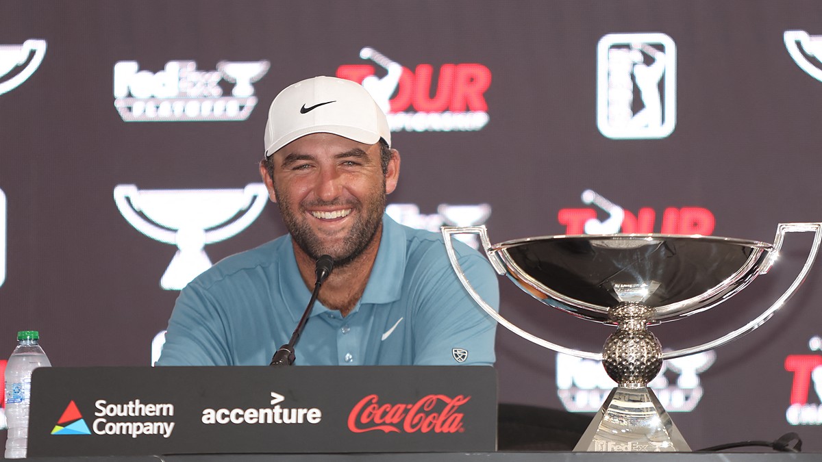 Scottie Scheffler smiles at a news conference podium next to the FedEx Cup trophy.