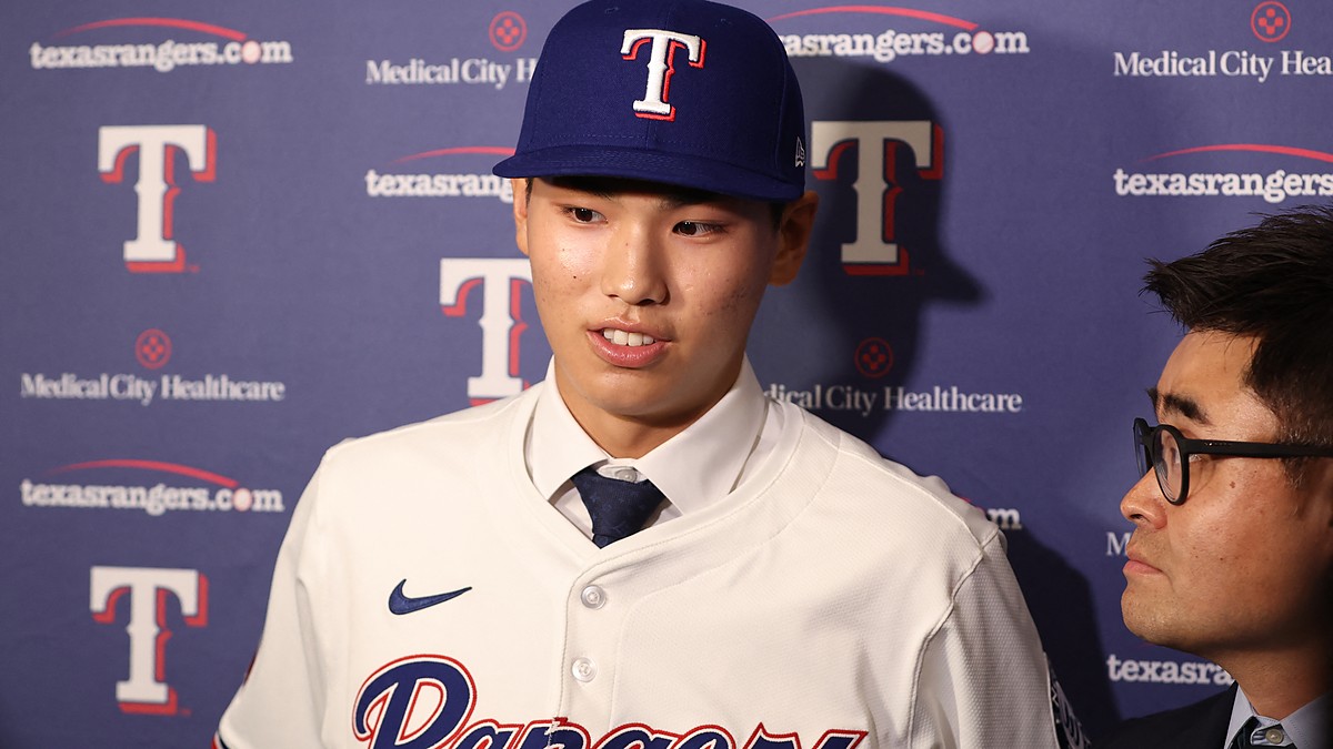 Texas Rangers two-way prospect Seong-Jun Kim speaks to reporters in a Rangers jersey and cap at Globe Life Field.