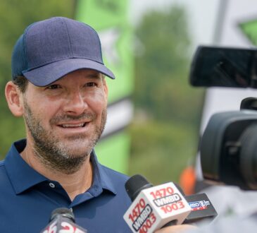 Former Dallas Cowboys quarterback Tony Romo smiles as he answers questions in front of television microphones.