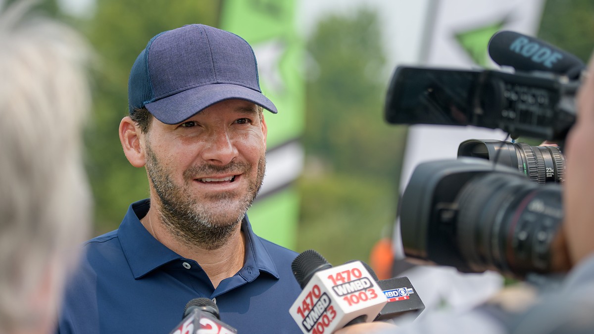 Former Dallas Cowboys quarterback Tony Romo smiles as he answers questions in front of television microphones.