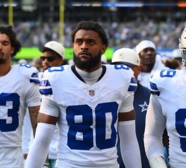 Dallas Cowboys wide receiver Traeshon Holden stands on the sideline in his white No. 80 jersey between two teammates.