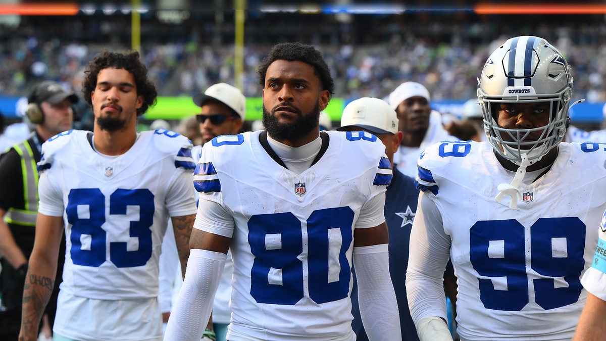 Dallas Cowboys wide receiver Traeshon Holden stands on the sideline in his white No. 80 jersey between two teammates.