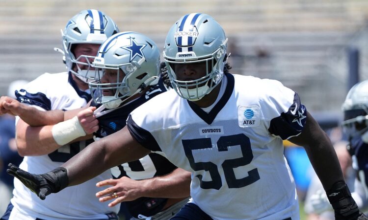Dallas Cowboys guard Tyler Booker extends his arms during a training camp drill in a No. 52 practice jersey.