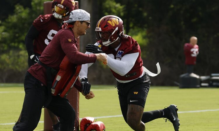 Washington Commanders linebacker Von Miller drives past a coach holding a blocking pad during a training camp drill.