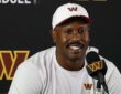 Washington Commanders outside linebacker Von Miller smiles while answering questions at a podium in a white team cap.