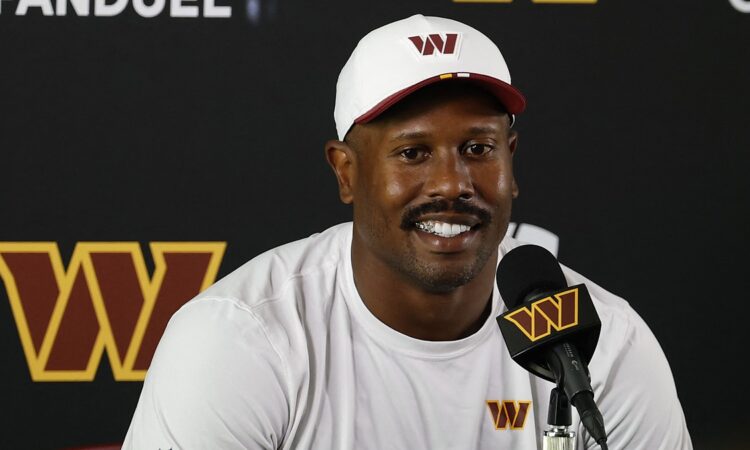 Washington Commanders outside linebacker Von Miller smiles while answering questions at a podium in a white team cap.