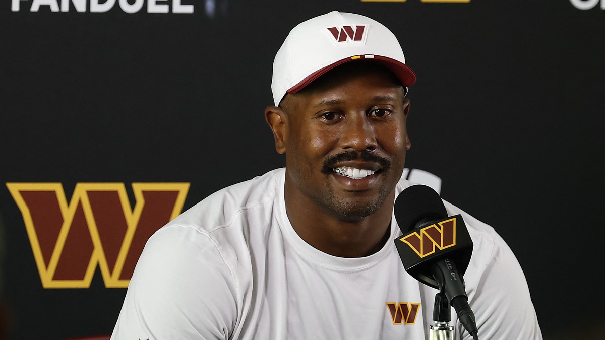 Washington Commanders outside linebacker Von Miller smiles while answering questions at a podium in a white team cap.