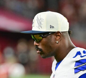 Dallas Cowboys edge rusher Von Miller looks on from the sideline in a cap and sunglasses at State Farm Stadium.