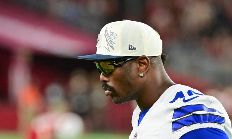 Dallas Cowboys edge rusher Von Miller looks on from the sideline in a cap and sunglasses at State Farm Stadium.