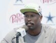 Von Miller sits at a podium microphone in a gray shirt and cream cap during a Cowboys press conference.