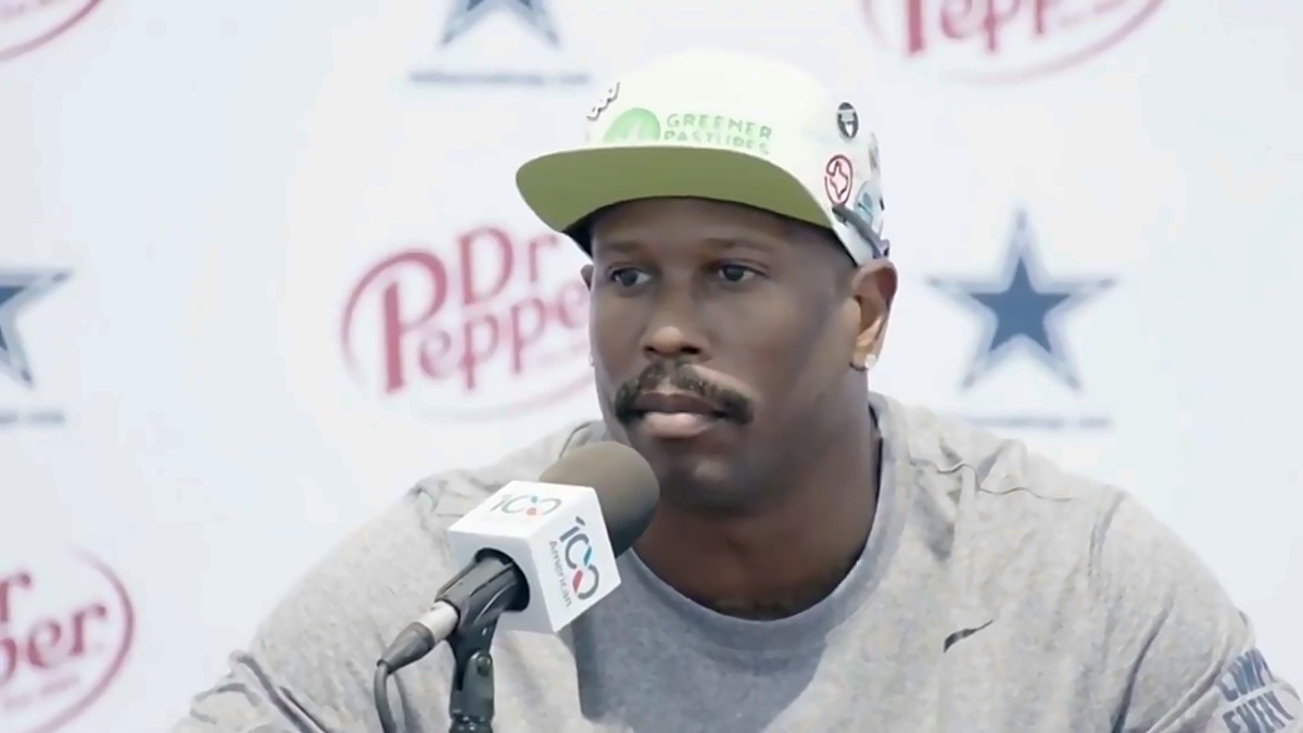 Von Miller sits at a podium microphone in a gray shirt and cream cap during a Cowboys press conference.