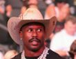 Von Miller looks on in a cream cowboy hat and diamond chains from the crowd at a UFC event.