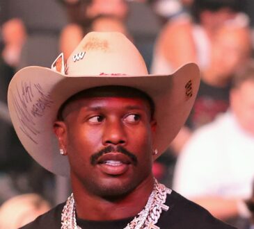 Von Miller looks on in a cream cowboy hat and diamond chains from the crowd at a UFC event.