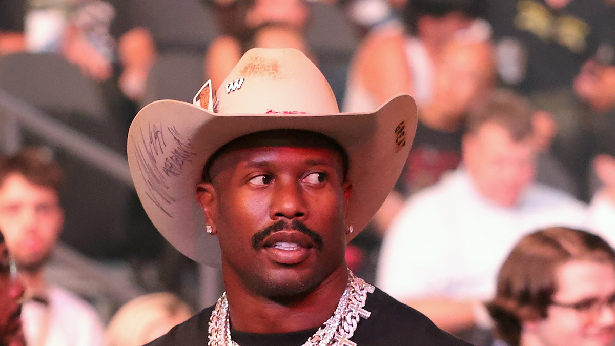 Von Miller looks on in a cream cowboy hat and diamond chains from the crowd at a UFC event.
