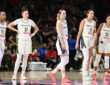 Dallas Wings guard Paige Bueckers and four teammates in white road uniforms stand on the court during a stoppage in play.