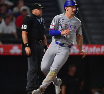 Texas Rangers left fielder Wyatt Langford jogs across the plate to score as the umpire watches behind him.