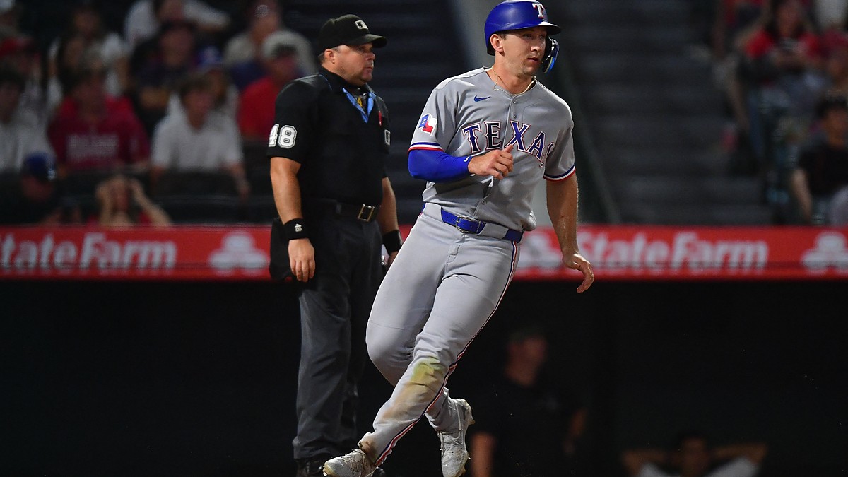 Texas Rangers left fielder Wyatt Langford jogs across the plate to score as the umpire watches behind him.