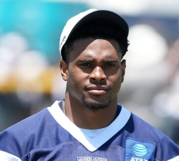 Dallas Cowboys cornerback Zion Childress looks toward the field in a navy practice jersey and white cap.