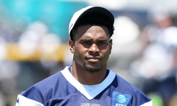 Dallas Cowboys cornerback Zion Childress looks toward the field in a navy practice jersey and white cap.