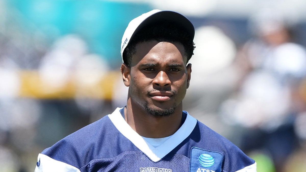 Dallas Cowboys cornerback Zion Childress looks toward the field in a navy practice jersey and white cap.