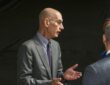 NBA commissioner Adam Silver gestures with both hands while talking with two men before the game.