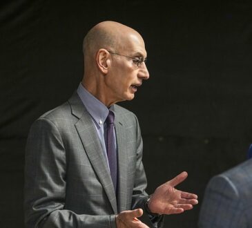 NBA commissioner Adam Silver gestures with both hands while talking with two men before the game.