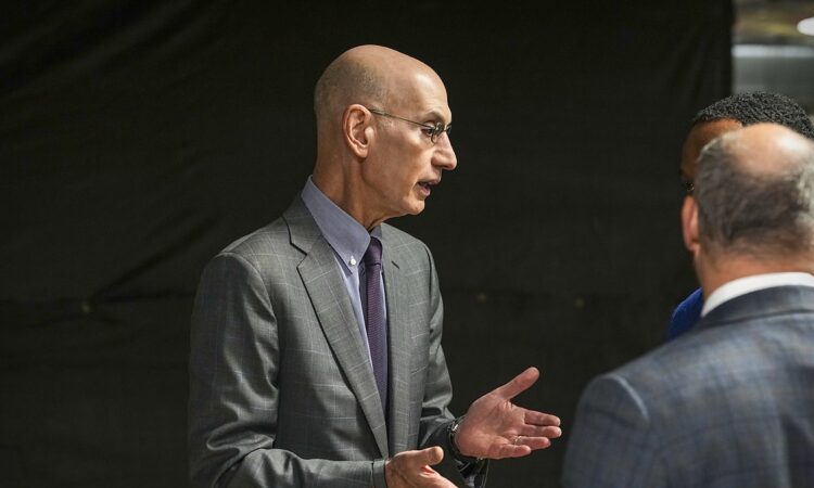 NBA commissioner Adam Silver gestures with both hands while talking with two men before the game.