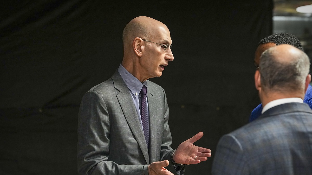 NBA commissioner Adam Silver gestures with both hands while talking with two men before the game.