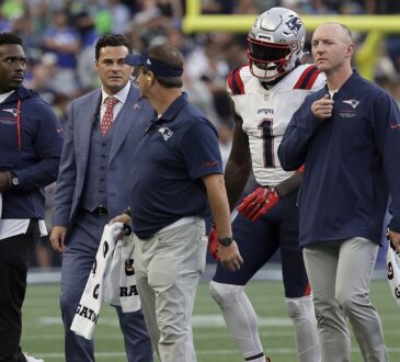 New England Patriots wide receiver A.J. Brown walks on the field alongside four Patriots staff members.