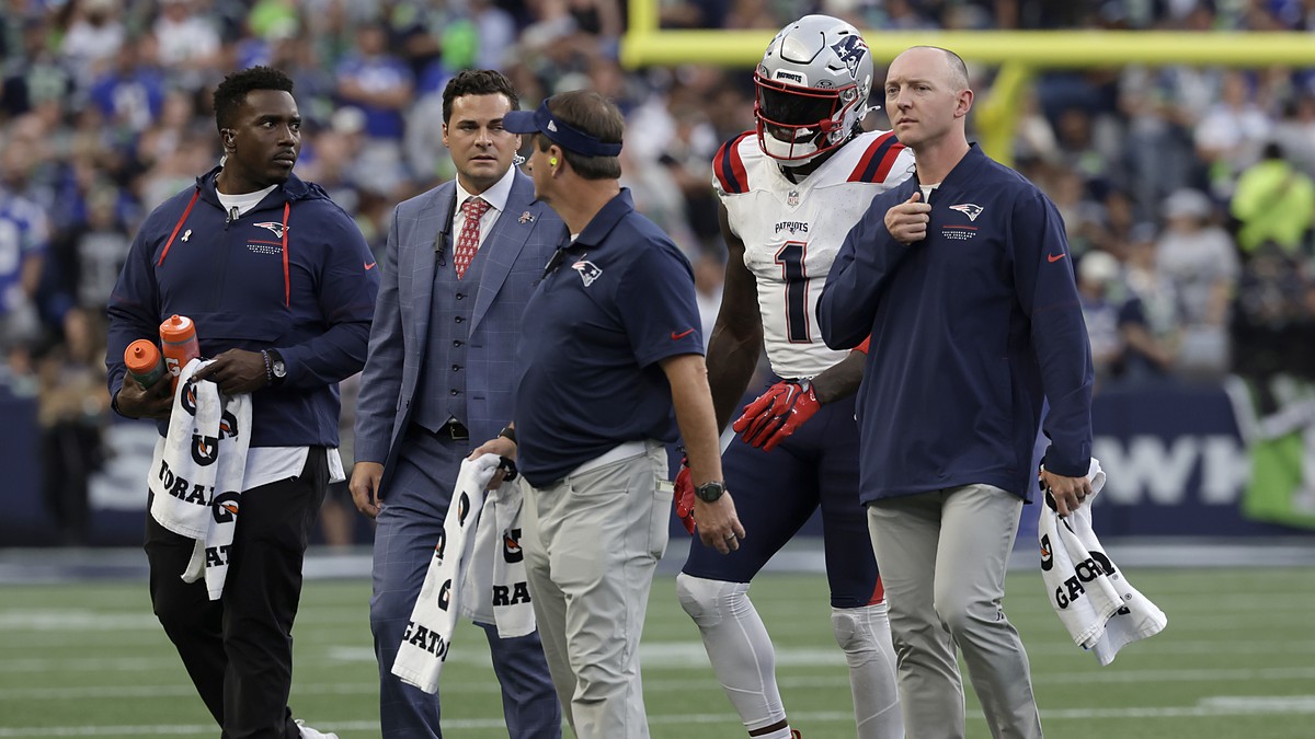 New England Patriots wide receiver A.J. Brown walks on the field alongside four Patriots staff members.