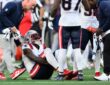New England Patriots wide receiver A.J. Brown sits on the field as a trainer and teammates gather around him.